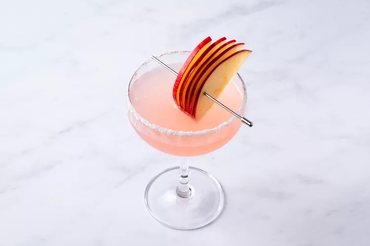 A pink appletini mocktail garnished with apple slices, which is one of the best non-alcoholic drinks for summer