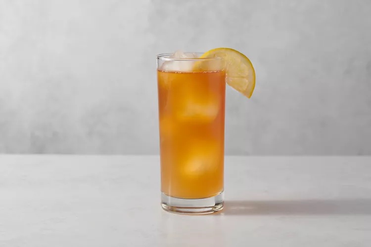 A glass containing an Arnold Palmer with a lemon wedge as a garnish