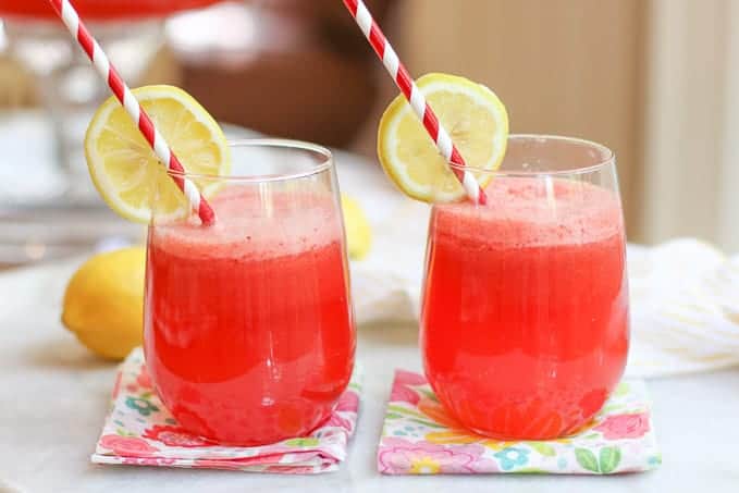 Two glasses of strawberry lemonade punch garnished with straws and lime slices