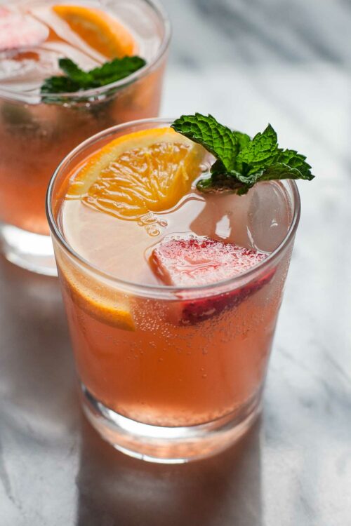 A glass of strawberry orange ginger fizz garnished with an orange and strawberry