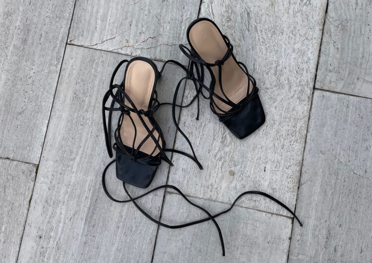 Black strappy heel sandals on a gray wooden floor
