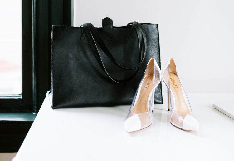 Clear high heels in front of a black bag