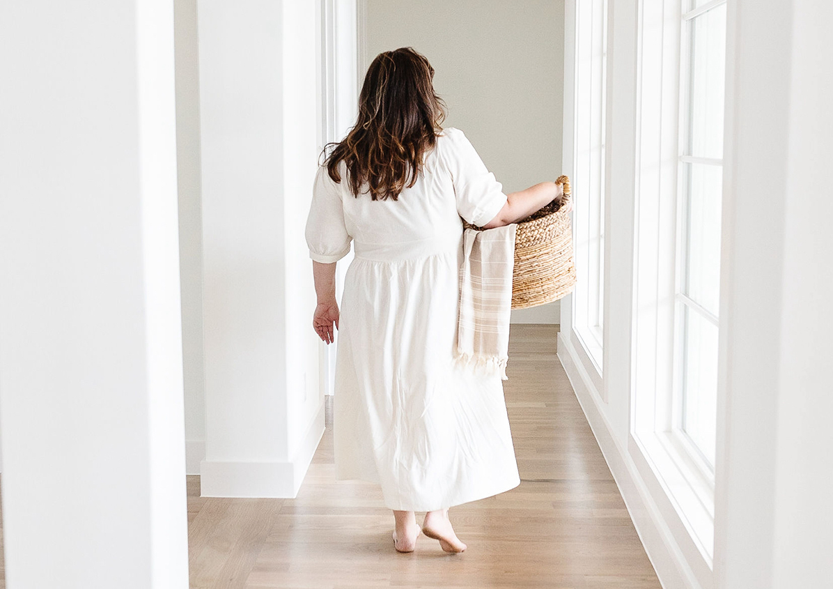 Person wearing a white dress walks down the hallway with a basket in their hand