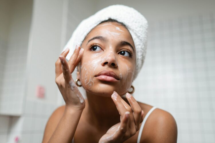 Person with their hair in a white towel takes care of their skin