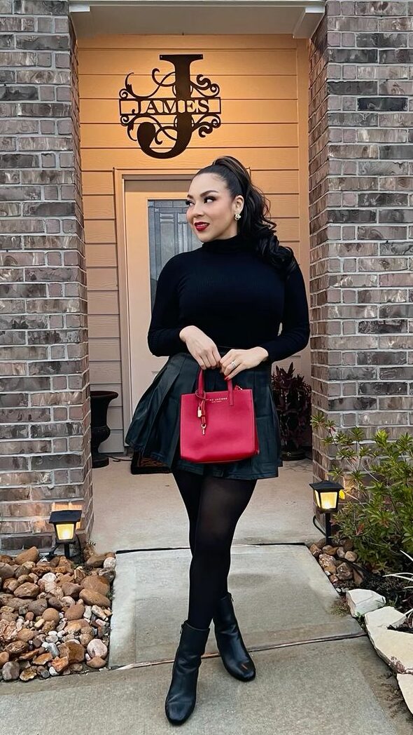 Someone in an all-black outfit holding a red purse and wearing a ponytail