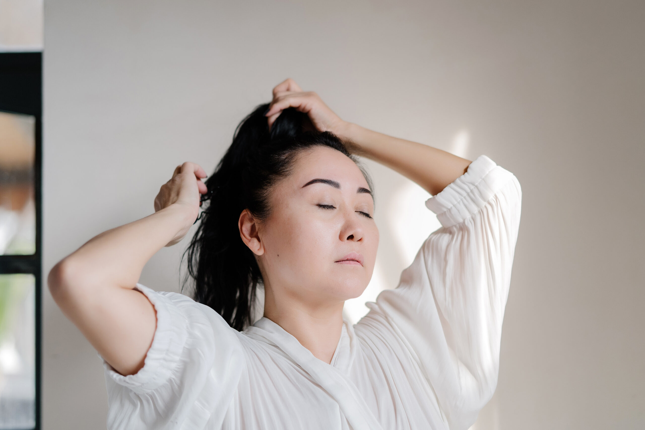 Person wearing a white shirt puts their hair up in a ponytail