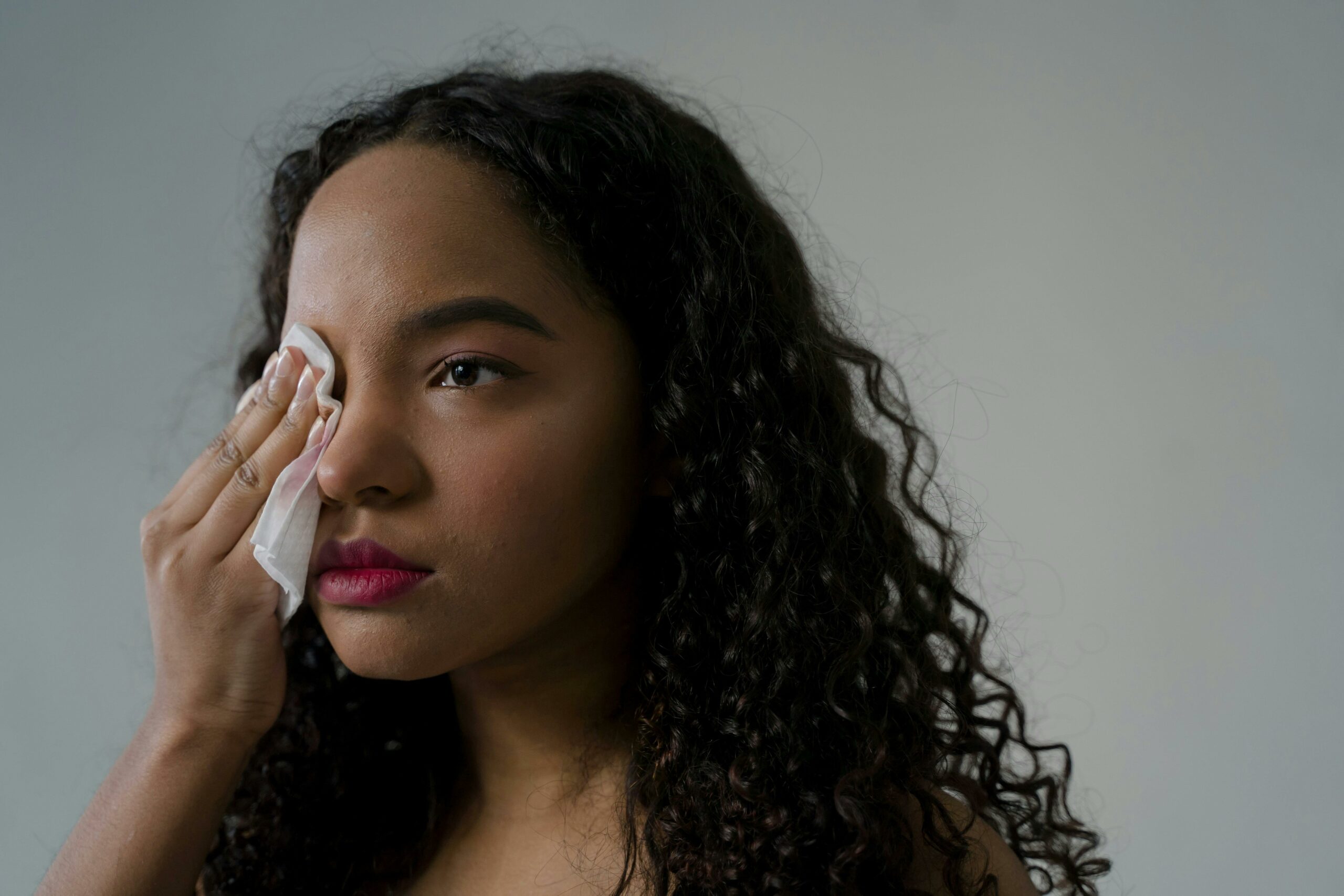 Person with curly hair using makeup wipes, which are bad for skin