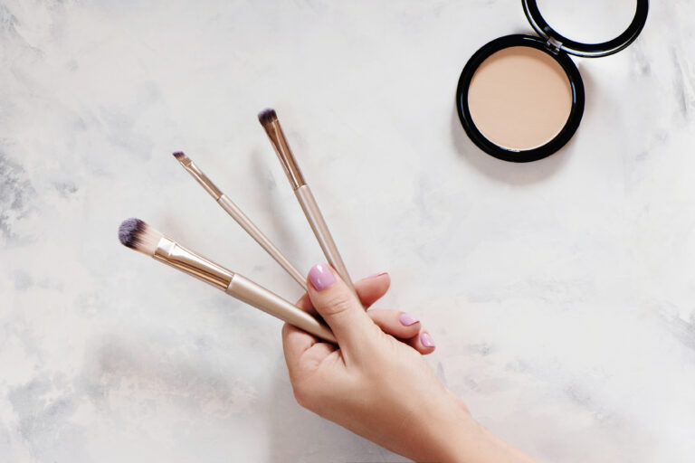 Person holding three makeup brushes in their left hand