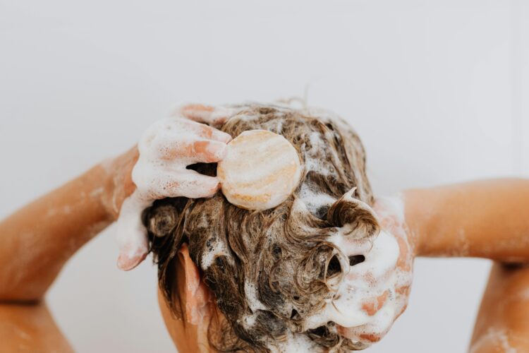 Person washing their hair in the shower while holding a shampoo bar