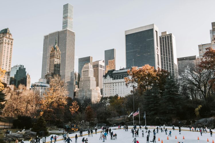 People ice skating in the park with buildings in the background