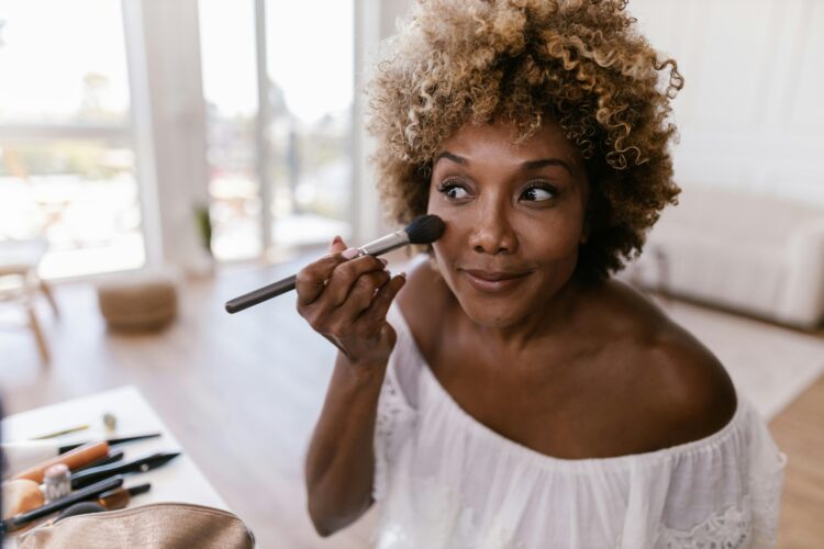 Person applying makeup with a big brush in the mirror