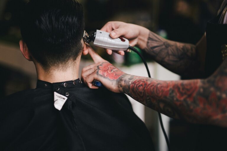 The back of someone's head as they're getting a haircut from a barber with tattoos